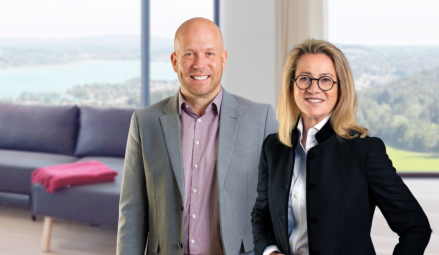 Petra Berger und Alexander Thamm, das Team der Mr. Lodge Filiale am Tegernsee, vor traumhafter Seelandschaft – Ihre Ansprechpartner für exklusive möblierte Immobilien in der Region.