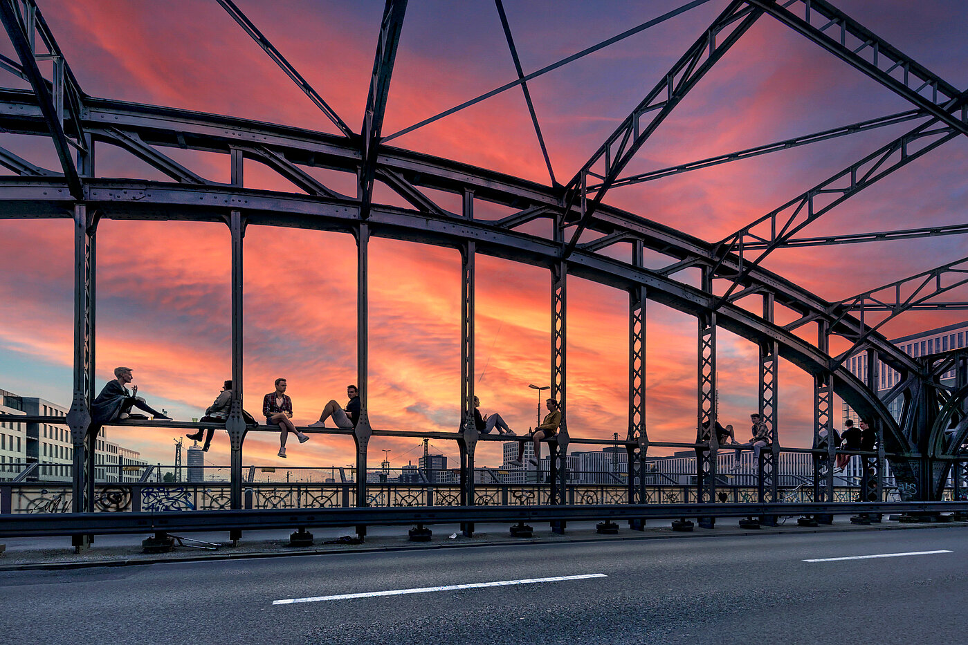 Zu sehen ist die Hackerbrücke, auf der zahlreiche Menschen sitzen, die sich den Sonnuntergang anschauen