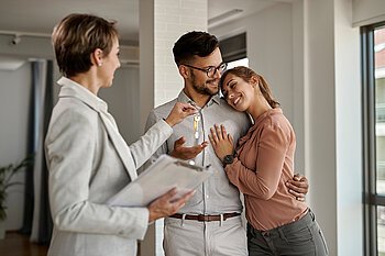 Glückliches Paar übernimmt symbolisch den Wohnungsschlüssel von Immobilienmaklerin – der perfekte Moment beim Kauf einer möblierten Immobilie mit Mr. Lodge in München.