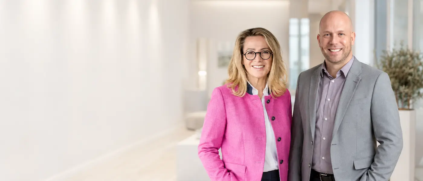 Petra und Alexander, Immobilienmakler am Tegernsee, lächeln in einem hellen Wohnraum