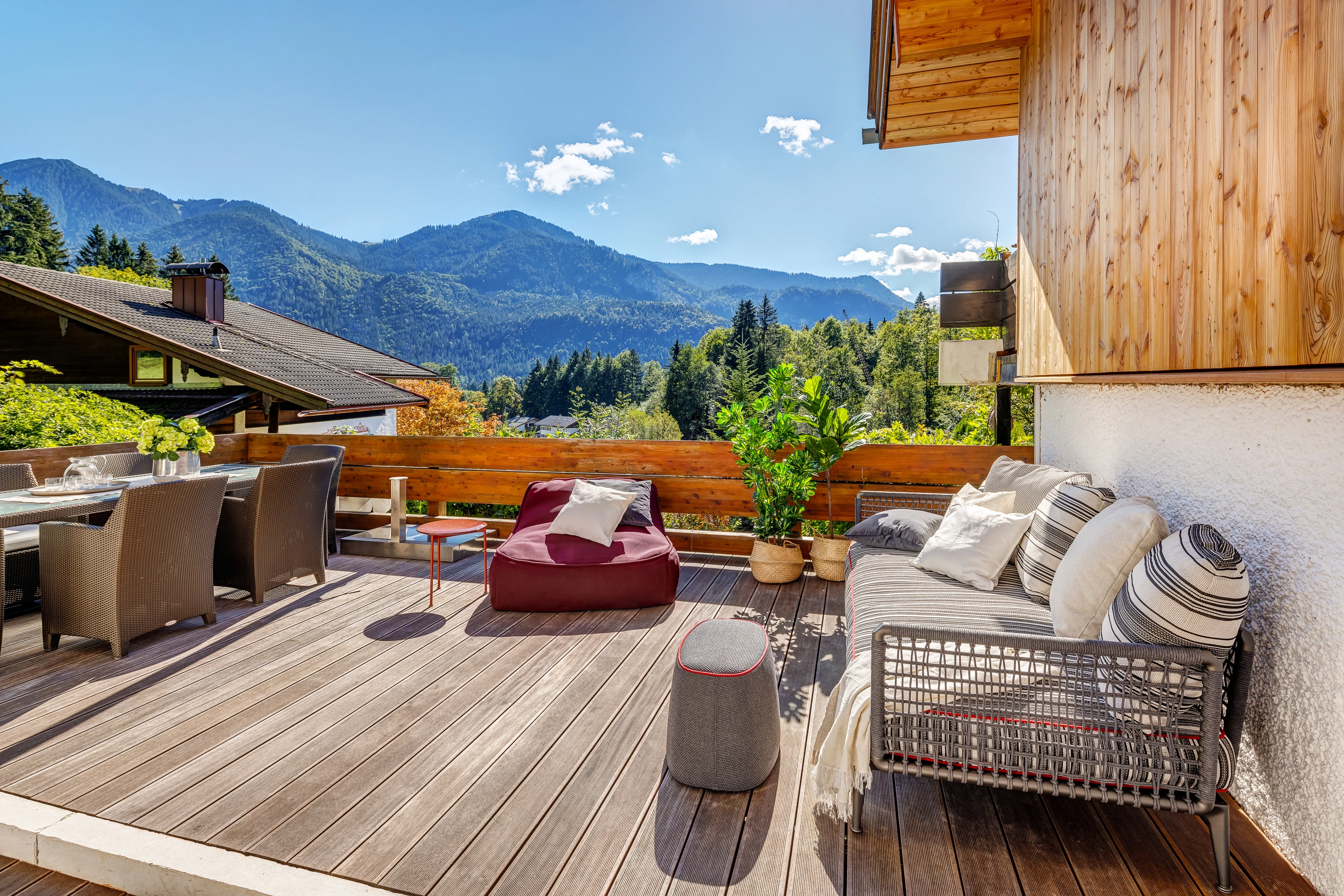 Sonnige Holzterrasse mit Loungemöbeln und Pflanzen, freier Blick auf die bayerischen Alpen